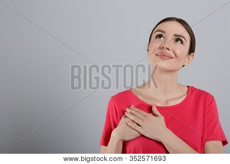 Beautiful Grateful Woman With Hands On Chest Against Light Grey Background. Space For Text