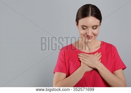 Beautiful Grateful Woman With Hands On Chest Against Light Grey Background. Space For Text