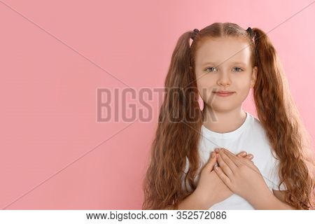 Cute Grateful Little Girl With Hands On Chest Against Pink Background. Space For Text