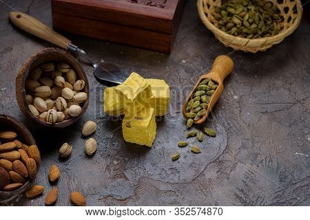 Cubed Pyramid Of Dessert Soan Papdi, Cardamom Grains In Wooden Scoop, Pistachios And Almond On Concr