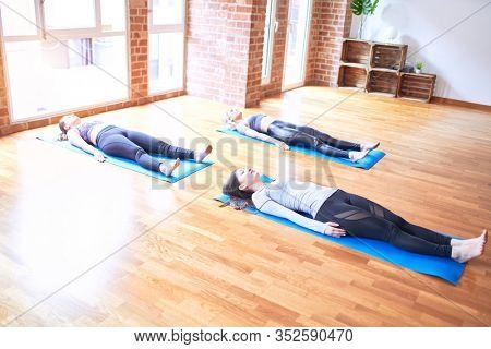 Young beautiful group of sportswomen smiling happy practicing yoga. Lying down doing corpse pose at gym
