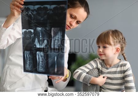 Portrait Of Smiling Girl Looking At X-ray With Interest And Gladness. Experienced Pediatrician Point
