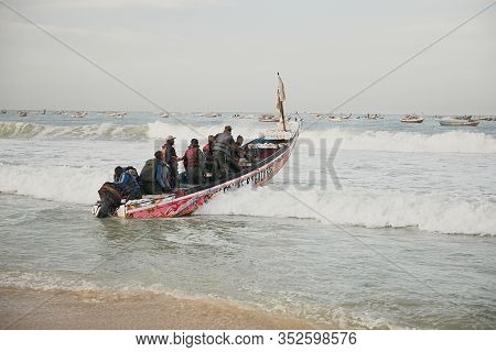 Kayar, Senegal - January 17, 2020: Fishermans Pushing Traditional Painted Wooden Fishing Boat In Kay