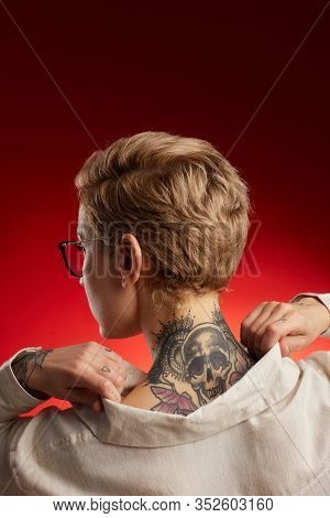 Back View Of Short Haired Young Woman With Neck Tattoo Featuring Scull And Butterflies Posing Agains
