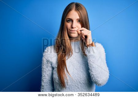 Young beautiful redhead woman wearing casual sweater over isolated blue background mouth and lips shut as zip with fingers. Secret and silent, taboo talking