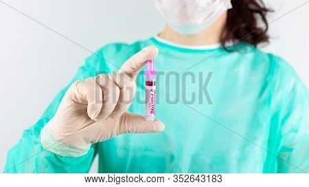 Nurse In Medical Green Coat, Gloves, Mask On White Background. Holds  Positive Blood Test In His Han