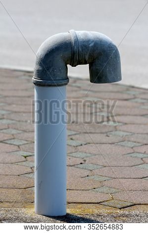 Plastic Candy Cane Shaped Vent Relief Pipe Sticking Out Of Concrete Foundation Surrounded With Stone