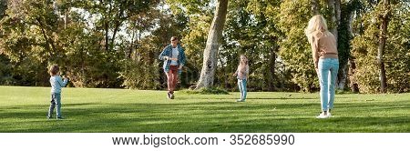 Full-length Portrait Of Happy Family Of Four Playing With Disc On A Green Meadow With Grass. Family,