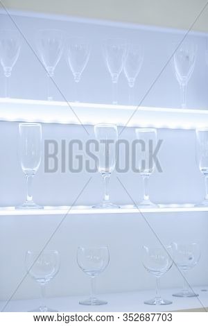 Clean Wine Glasses And Champagne Flutes Upended On A White Wooden Shelf In A Kitchen Or Bar
