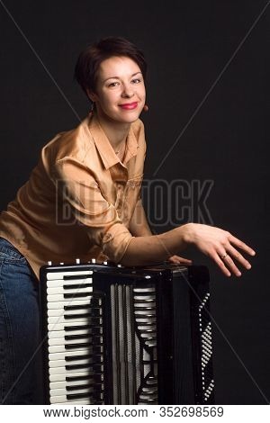 A Brunette In A Gold Shirt, With Short Haircut, On A Dark Kground Of The Studio. With Accordion Musi