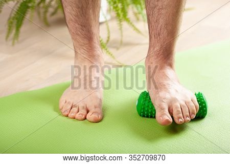 man doing flatfoot correction gymnastic exercise using massage roller at home
