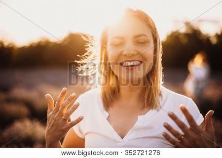 Charming Caucasian Mother Smiling And Gesturing Against The Sunshine With A Lavender Field On Backgr