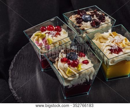 Group Of Trapezoid Clear Glasses With Layered Dessert Of Different Flavors On Black Round Board