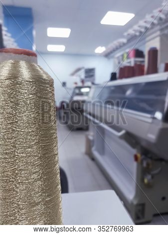 Shiny Thread On A Cone Against The Background Of Modern Knitting Machines.
