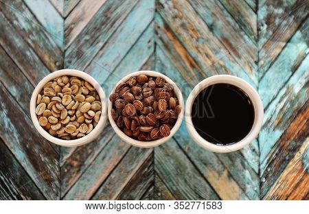 Green Raw Beans, Roasted Coffee Beans And Black Coffee In Three White Cups On Turquoise Wooden Backg