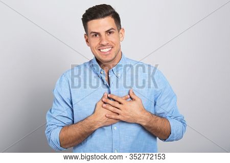 Handsome Grateful Man With Hands On Chest Against Light Grey Background