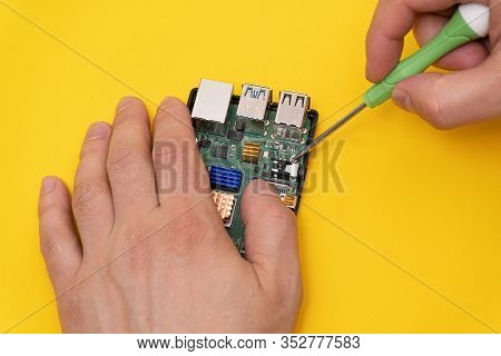 Man Fixes Circuit Board In Microcomputer With Screwdriver With Green Handle On Yellow Background, Cl