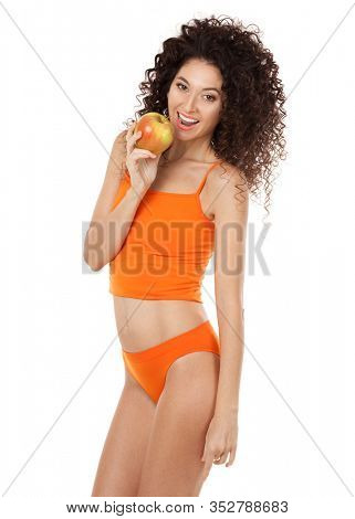 Cute curly woman with beautiful snow-white smile in orange lingerie holding big apple. Healthy lifestyle and nutrition, dieting, weight loss, cosmetology, dental care and healthy teeth con?ept