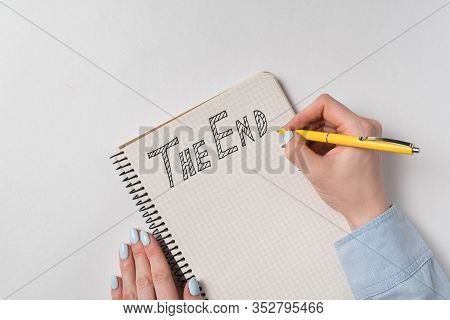 Handwritten Note The End. Female Hand Writing Text In Notepad. White Background Top View.