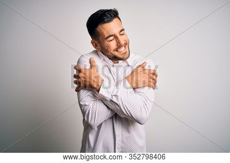 Young handsome man wearing elegant shirt standing over isolated white background Hugging oneself happy and positive, smiling confident. Self love and self care