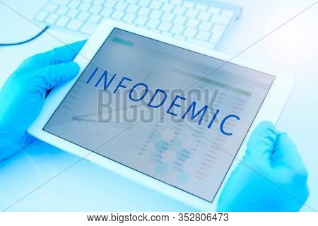 closeup of a doctor man, wearing blue surgical gloves, having a digital tablet in his hands with the word infodemic in its screen