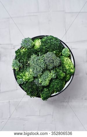 high angle view of some stems of raw broccoli in a bowl, on a white textured surface