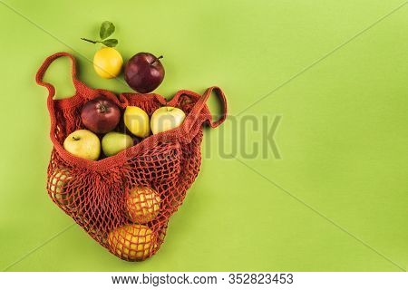 Apples And Lemons In An Orange String Bag On A Green Background. Top View. Concept Of Life Without P