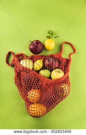 Apples And Lemons In An Orange String Bag On A Green Background. Top View. Concept Of Life Without P