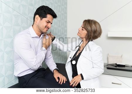 Senior Female Physician Examining Mid Adult Man Suffering From Joint Pain In Clinic