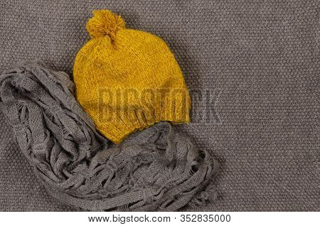Yellow Mustard Beret With Pampon And Gray Scarf On A Gray Knitted Background