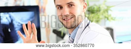 Portrait Of Smiling Doc Posing In Hospital Cabinet. Smiling Surgeon Wearing Medical Coat. X-ray Pict