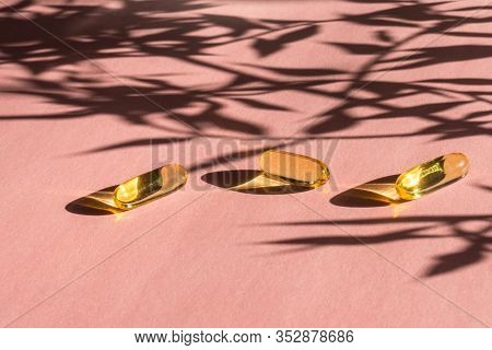 Oil Yellow Gelatin Capsules On Pink Background With Flower Shadow, Vitamins And Antioxidant Concept 
