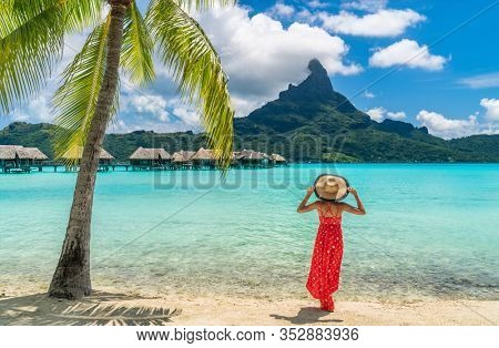 Luxury beach vacation travel destination tourist woman walking on Bora Bora island enjoying holiday in Tahiti, French Polynesia with Mount Otemanu and overwater bungalows villas hotel landscape.