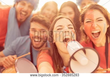 Football Fan Screaming, With Red Shirts In The Stadium . Group Of Young People Very Excited About Fo