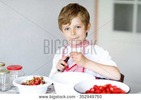 Healthy Little Blond Kid Boy Helping And Making Strawberry Jam In Summer. Funny Child Cleaning Berri