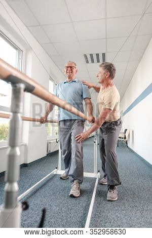 Physiotherapist woman helping senior man in rehabilitation walking on the bars