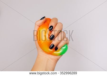 Hands With Black Manicure Holding Slime In Orange And Green Vibrant Colors