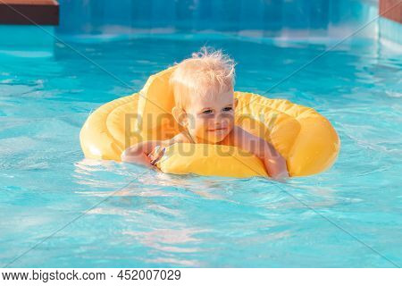 Toddler Boy Swimming With Inflatable Floatie In Swimming Pool On A Sunny Day.