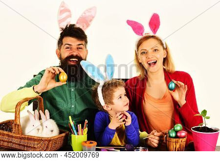 Happy Family With Easter Colorful Eggs. Mother, Father And Son In Bunny Ears Sit At Wooden Table.
