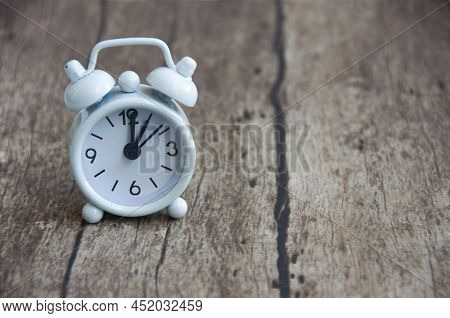White Alarm Clock Isolated On Wooden Desk. The Clock Set At 1 O\'clock. Deadline Concept.