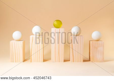Prominent Yellow Sphere Among White Spheres On Wooden Bars On Pastel Beige Background. Difference In