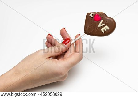 A Woman's Hand Holds A Candy On A Stick In The Form Of A Heart. High Quality Photo