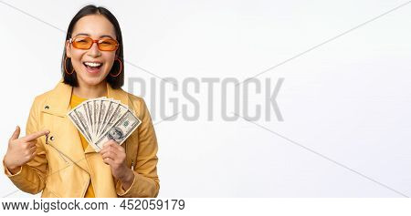 Microcredit And Money Concept. Stylish Asian Young Woman In Sunglasses, Laughing Happy, Holding Doll
