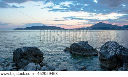 Blue Seascape With Stoney Beach At Sunset. Stone Coastline With Islands On The Skyline For Publicati
