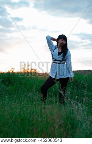 Young Woman In Baldric On The Summer Field On Sunset Or Sunrise. Peaceful Calm Female. Trendy Clothe