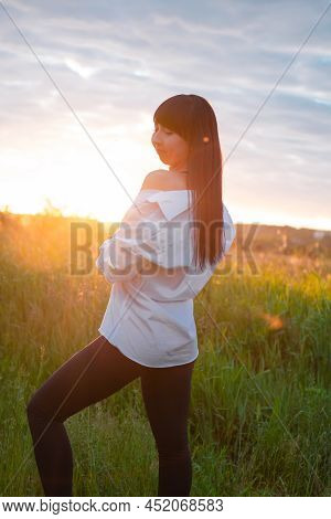 Young Woman In Baldric On The Summer Field On Sunset Or Sunrise. Peaceful Calm Female. Trendy Clothe