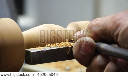 Man Carpenter Using Chisel For Shaping Piece Of Wood On Turning Lathe Machine With Many Shavings At 