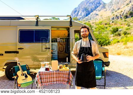 Man In Charming Trailer House Makes Coffee Outdoors In Mountains In Summer Sunny Day