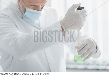 Scientist In Medical Mask And Latex Gloves Holding Micropipette And Flask With Liquid.