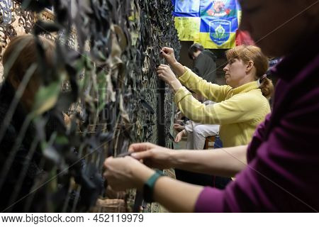 Kyiv, Ukraine - Apr. 01, 2022: A Group Of Volunteers In A Shelter Making Camouflage Net, From Differ